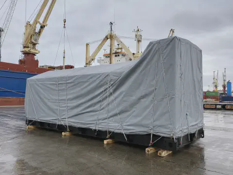 Gray tarpaulin cover protecting a generator set during port loading
