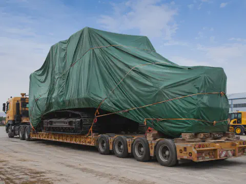 Green tarpaulin cover protecting an excavator on lowbed transport